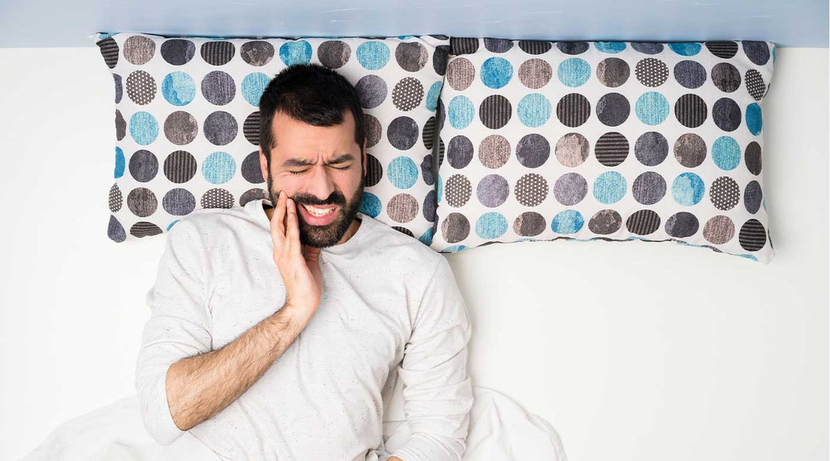 Mann liegt schlaflos im Bett, hält sich den Kiefer